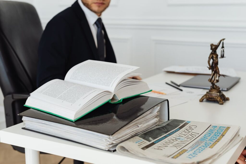 pexels-photo-7876088-7876088 A lawyer sitting at a desk with legal books, documents, and a newspaper, embodying professionalism.